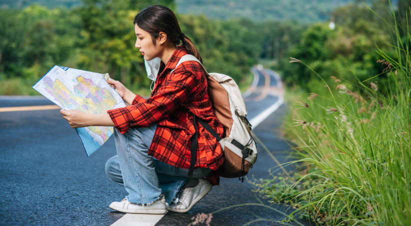 Solo female traveler with backpack reading map on scenic road during independent travel adventure.