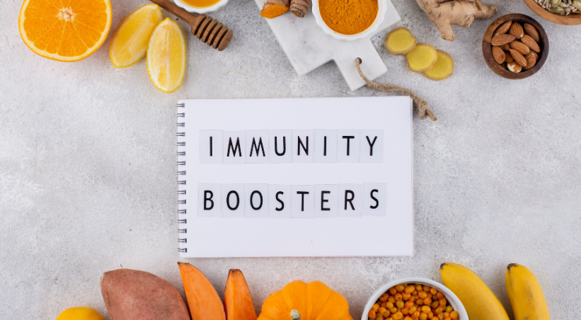 Immune system booster foods including oranges, lemons, ginger, turmeric, almonds and sweet potatoes arranged around immunity boosters notebook on marble surface.