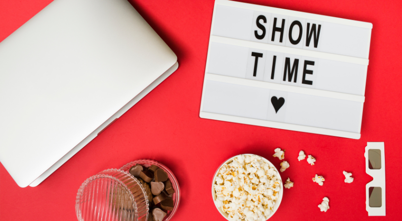 Laptop with popcorn and chocolates on red background showing showtime sign for watching best Netflix series of all time.